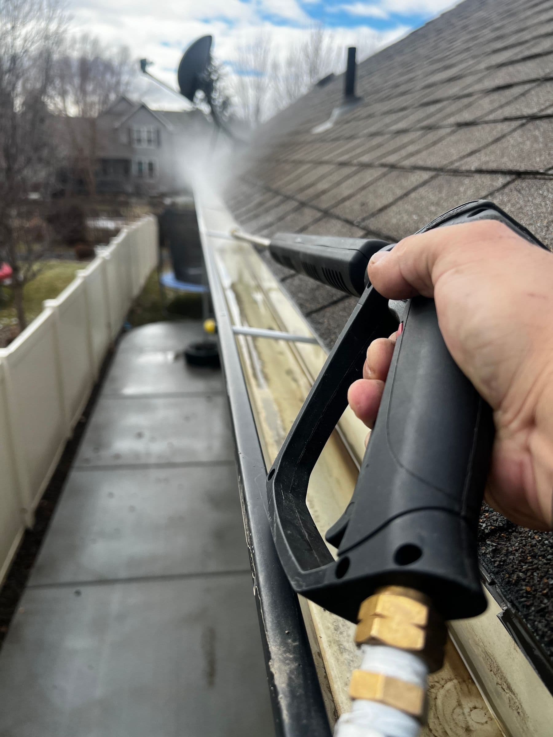 Close-up of an eavestrough being cleaned along a shingled roofline